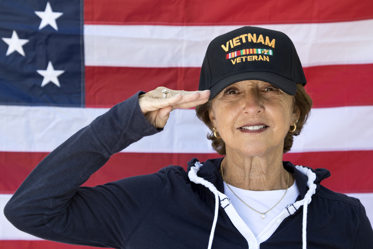 A woman Vietnam-era veteran saluting in front of an American flag